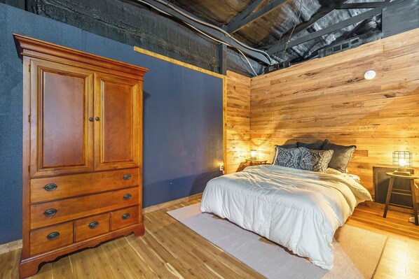 Un dormitorio con un armario de madera, una cama con ropa de cama blanca y una mesita de noche con una lámpara.