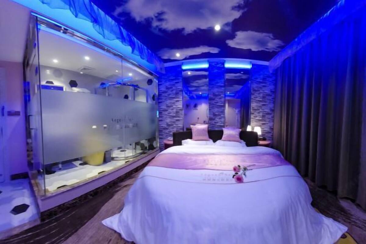 A bedroom with a large bed, a glass partition, and a stone wall.