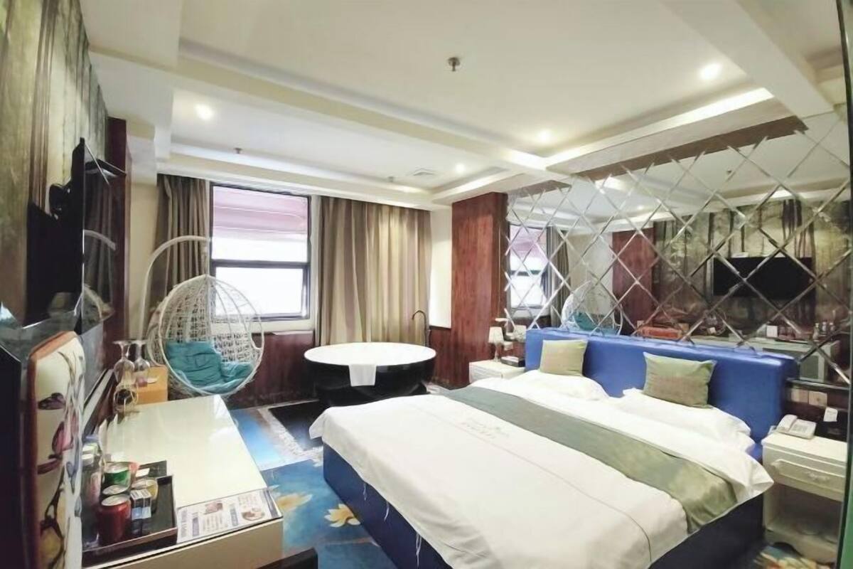 A hotel room with a bed, a round table, a hanging chair, a TV, and a window with curtains.
