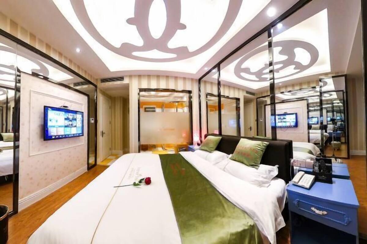 A hotel room with a large bed, a TV on the wall, and a mirror reflecting the room.