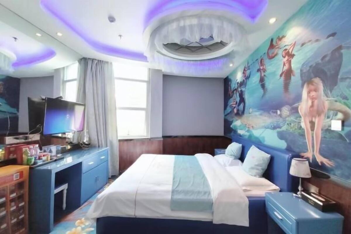 A hotel room with a bed, a TV, a desk, and a mural on the wall.