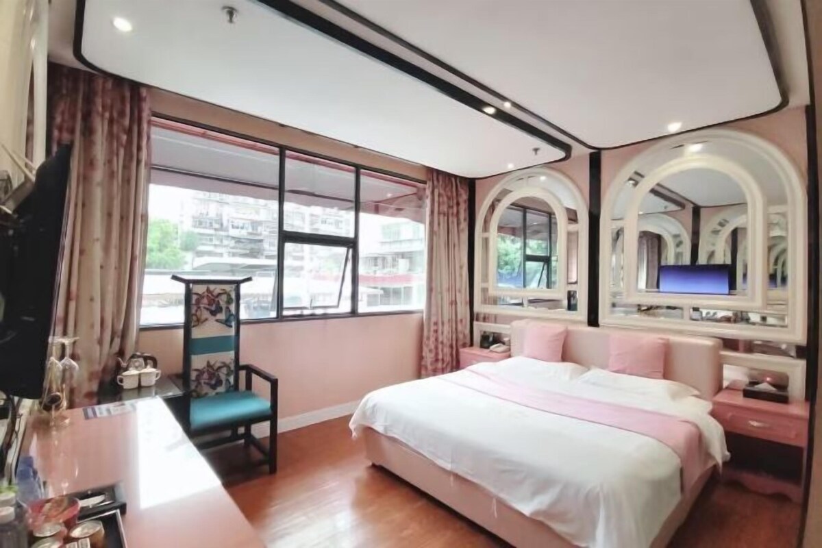 A bedroom with a bed, a TV, a desk with a chair, and a window with curtains.