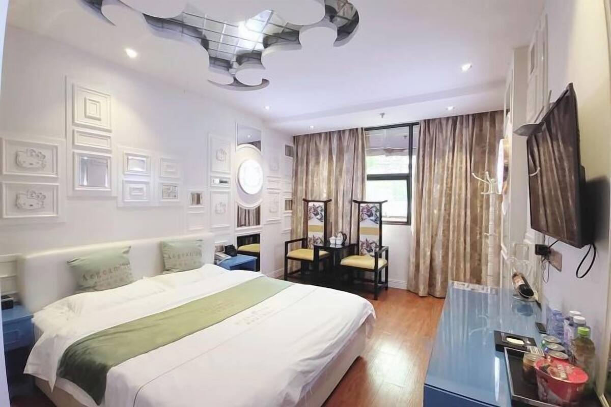 A hotel room with a bed, bedside table, chair, desk, and a TV.