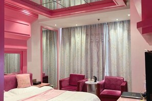 A hotel room with a bed, two chairs, a small table, and a large window with curtains.