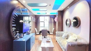 A modern living room with a flat-screen TV, a coffee table, a sofa, and a dining area with chairs. - Aegean Sea Theme Hotel (Nanping)