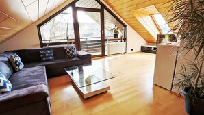 A modern loft with a sloped ceiling, a glass dining table, a sofa with patterned cushions, and a potted plant. - Studio apartment "SchwabenALB" with panoramic view (Albstadt)