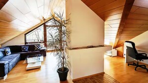 A modern loft with a sloped ceiling, a black office chair, a black sofa, a glass coffee table, and a potted plant. - Studio apartment "SchwabenALB" with panoramic view (Albstadt)