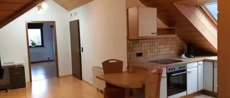 Une cuisine de taille réduite comprenant une table et des chaises, un fourneau et une fenêtre.