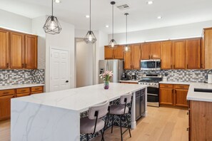 Une cuisine moderne avec des meubles en bois, un îlot en marbre, des luminaires suspendus et des appareils électroménagers en acier inoxydable.