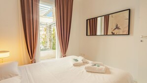 Une chambre d’hôtel avec un lit, une fenêtre avec des rideaux, un tableau accroché au mur et une lampe.