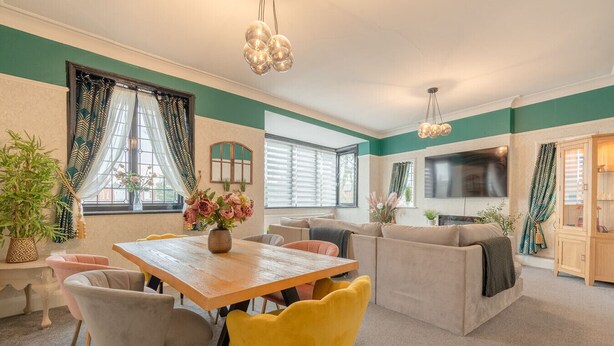 Un salon moderne avec une table à manger en bois, des chaises jaunes, un canapé beige et un téléviseur fixé au mur.