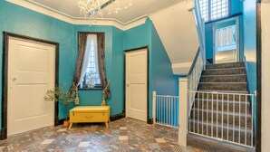 Un couloir aux murs de couleur turquoise, un sol à motifs, un banc jaune et un escalier doté d’une rampe.