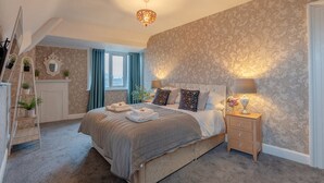 Une chambre avec un grand lit, une table de chevet, une commode, une échelle et une fenêtre avec des rideaux.