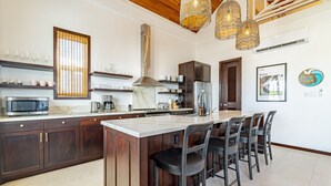 A modern kitchen with dark wood cabinets, a marble countertop, and a central island with bar stools. - Casa Playa Denver &Mistico Beach Club+Boat Shuttle (San Pedro)