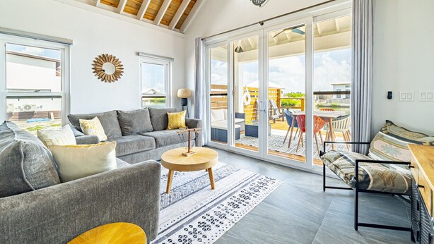 En rummelig stue med en grå sofa, et rundt træbord og en stor skydedør til en udendørs terrasse.