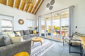 Een ruime woonkamer met een grijze bank, een ronde houten salontafel en een grote schuifpui naar een terras.