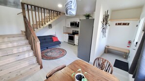 Une cuisine moderne équipée d’un four à micro-ondes, d’un four et d’un réfrigérateur. On y trouve une table à manger avec des chaises et une petite plante en pot. Un escalier avec des rampes en bois mène à un autre niveau.