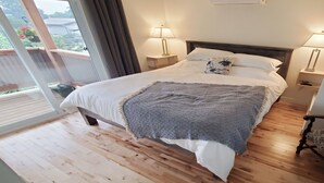 Une chambre avec un plancher en bois, un lit recouvert de draps blancs, un plaid à motifs et deux lampes de chevet.