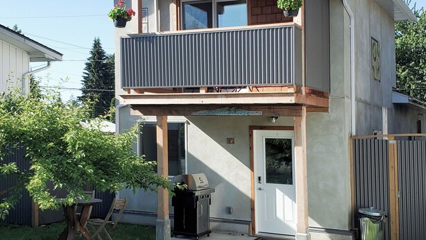 Une maison à deux étages avec un balcon, un barbecue à l’extérieur et une cour clôturée.