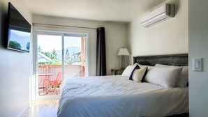 Une chambre d’hôtel avec un lit, un téléviseur fixé au mur et une porte-fenêtre coulissante donnant sur un espace extérieur comprenant une terrasse et des chaises.