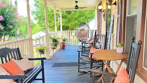 A covered porch with wooden flooring, a ceiling fan, and outdoor seating including a swing chair and chairs with cushions. - NEW-Heart of Kannapolis-Modern & Charming Escape (Kannapolis)