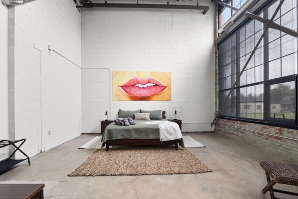A bedroom with a large window, a bed with a green bedspread, and a wall-mounted artwork of lips. - Historic Newark Station- 10% off Earthworks Cafe (Newark)