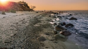 A beach with a rocky shoreline, a clear sky, and the sun setting on the horizon. - Apartment BeltEck - sea view. Sauna. Family-friendly. Dogs on request (Fehmarn)
