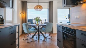 A modern kitchen with a dining area, featuring a large window, wooden flooring, and contemporary appliances. - Apartment BeltEck - sea view. Sauna. Family-friendly. Dogs on request (Fehmarn)