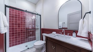Et moderne badeværelse med bruseniche i glas, et hvidt toilet, en vaskebord med vask og et spejl.