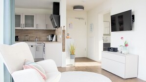 Ein modernes Wohnzimmer mit einem weißen Sessel, einem runden Couchtisch und einer Küchenzeile mit weißen Schränken und einem eingebauten Backofen.