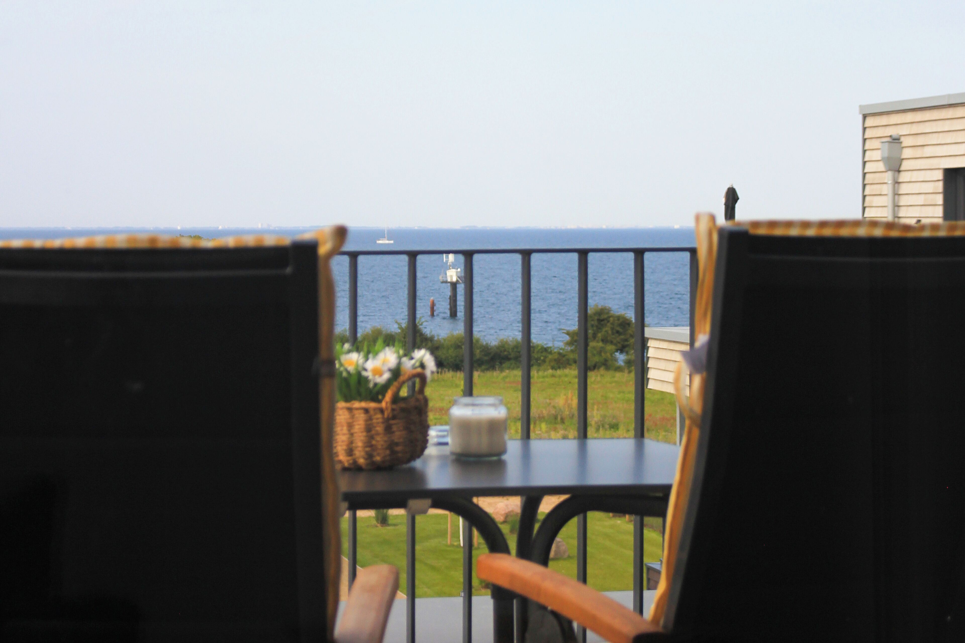 Un balcon avec des fauteuils en osier et une table, donnant sur un espace verdoyant et la mer.