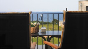 Ein Balkon mit Korbstühlen und einem Tisch, der auf eine Grünfläche und das Meer blickt.