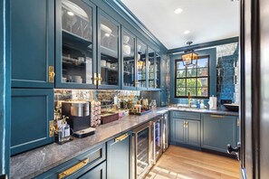 Une cuisine avec des meubles de couleur bleu foncé, une machine à café en acier inoxydable et une fenêtre donnant sur un paysage verdoyant.