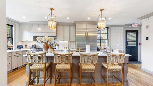 A modern kitchen with white cabinetry, stainless steel appliances, and a central island with bar stools.