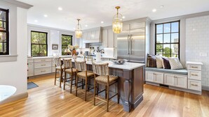 A modern kitchen with a central island, bar stools, and a built-in bench with cushions.