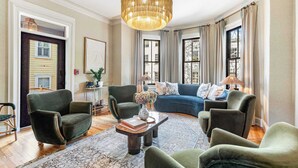 A living room with a large chandelier, a blue sofa, and green armchairs.