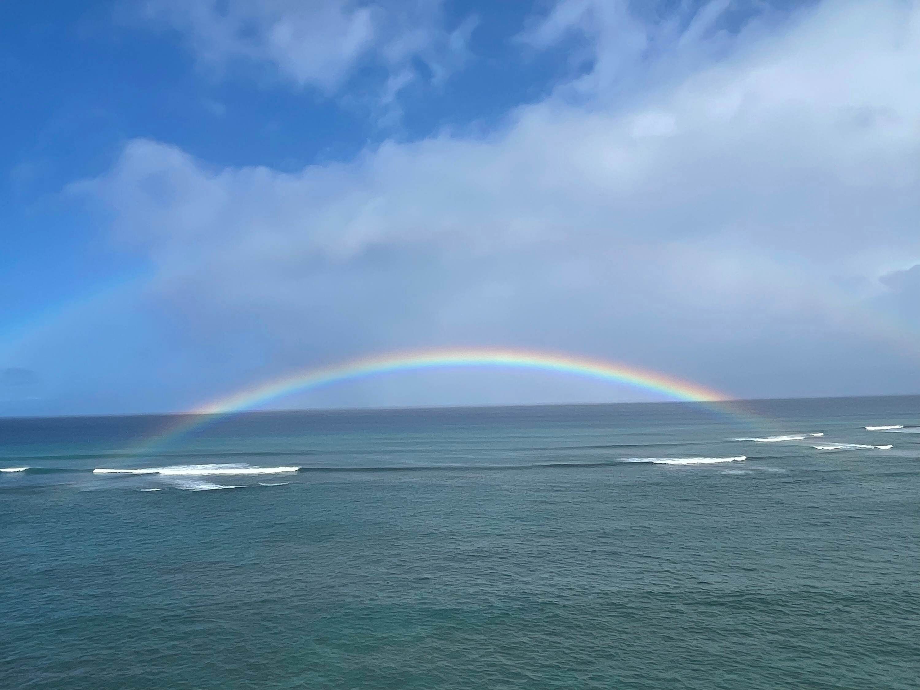 A clear view of the ocean with a rainbow arching over the water.