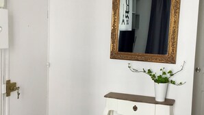 Eine weiße Tür mit Messingbeschlägen, ein weißer Konsolentisch mit einer Schublade, ein spiegel mit goldener Rahmen und ein Blumentopf auf dem Konsolentisch.