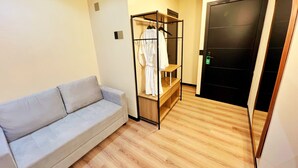Una habitación con un sofá gris, una estantería de madera con ropa y una puerta negra.