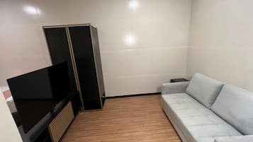 Ett vardagsrum med en platt-TV, en grå soffa och ett trägolv.