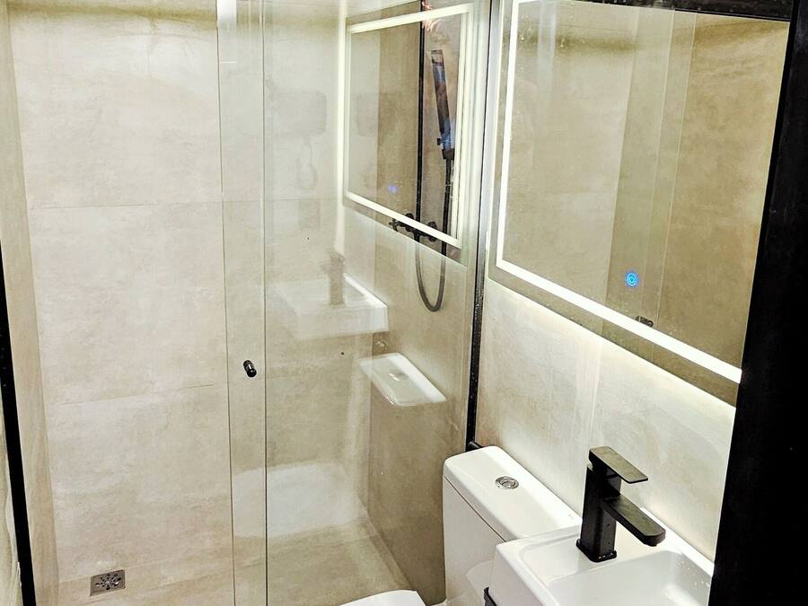 Une salle de bain moderne avec une douche à parois de verre, des toilettes blanches et un meuble-lavabo avec un miroir.