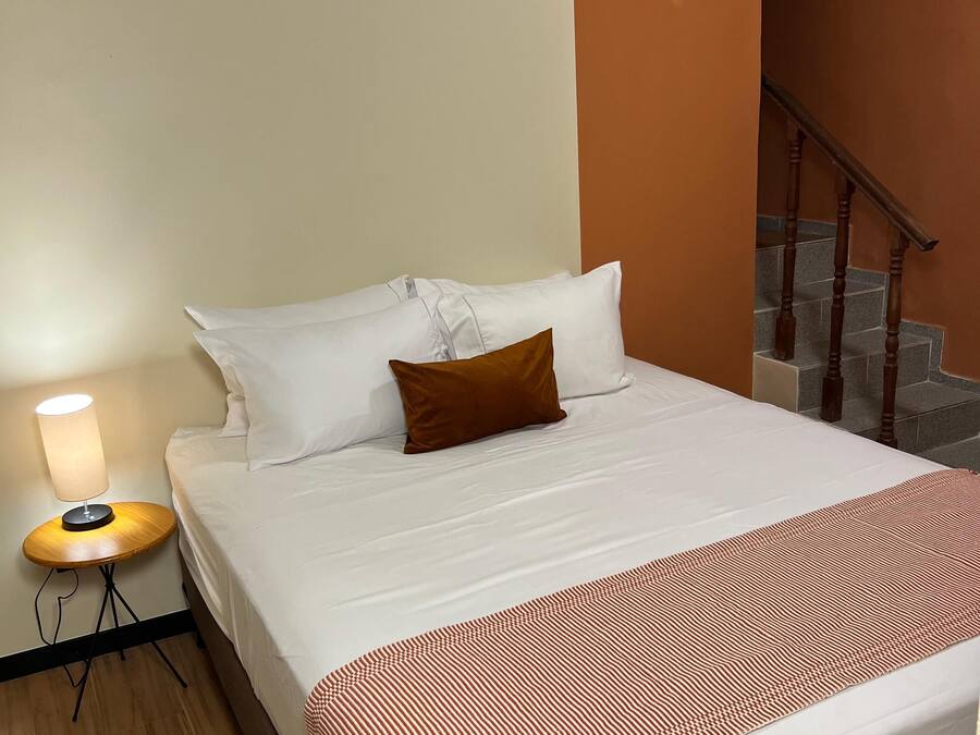 Una habitación de hotel con cama, lámpara de noche, aire acondicionado y una escalera.