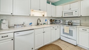 Una cocina con armarios blancos, cafetera, microondas, tostadora y hervidor.