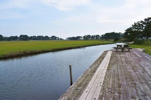 A wooden dock extending into a calm river, with a picnic table and benches on the right side.
