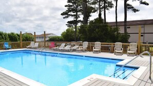 Une piscine avec une terrasse en bois, des chaises longues et une clôture en bois.