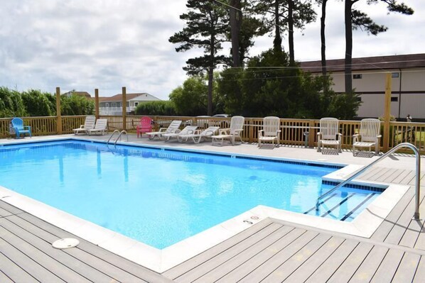 A swimming pool with a wooden deck, lounge chairs, and a wooden fence.