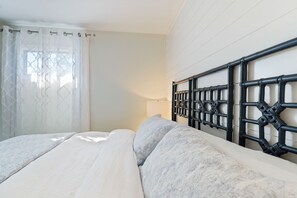 A bedroom with a bed, a headboard, a window with curtains, and a wall-mounted lamp.