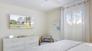 Une chambre à coucher avec un lit, une commode, une chaise et deux tableaux encadrés accrochés au mur.