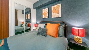 Une chambre moderne avec un grand lit, un miroir et des œuvres d’art accrochées au mur.