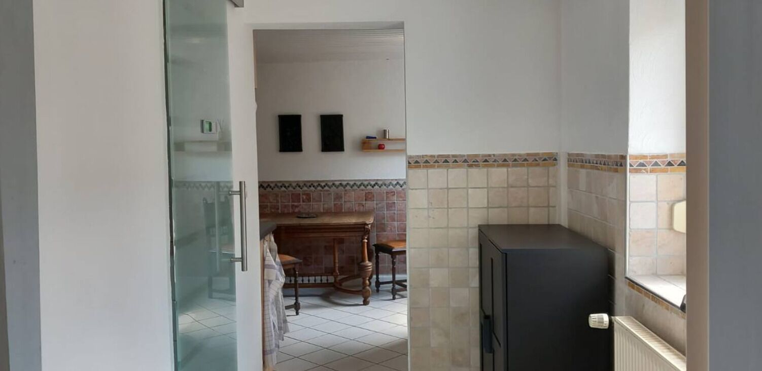 A narrow hallway with a glass door leading to a bathroom, a tiled wall with a decorative border, and a small wooden table with chairs.